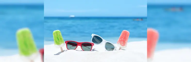 Glasses and ice lollies in the sand on a beach.